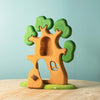 The Bumbu Handmade Wooden Ancient Oak Tree with Owl Set features a sustainable oak treehouse on a green base, with detailed foliage, a hollow trunk and small door, white flower accents, and an owl—perfect for imaginative play.