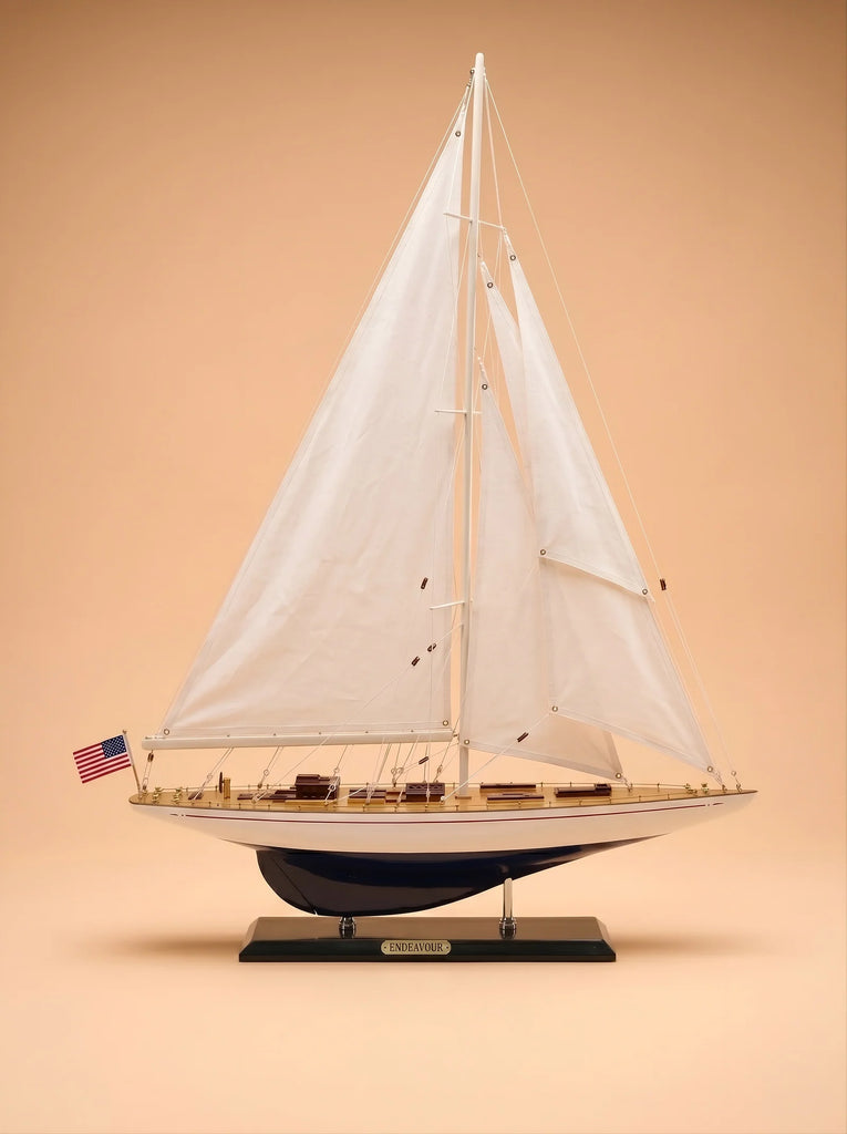 A detailed handcrafted "Little Forest Animals Silk Rug — The Regatta Series — The Endeavour," featuring elegant depictions of sailing yachts with white sails and a small American flag on the stern, displayed against a plain beige background.