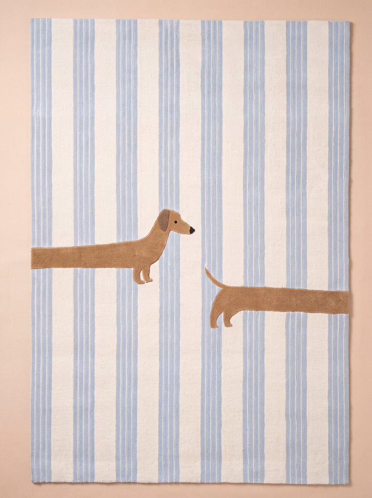 The Little Forest Animals Silk Rug — The Dachshund showcases a playful dachshund stretched across blue and white stripes, with its head and front legs on the left and its tail and back legs on the right—a charming hand-tufted silk rug that’s perfect for a children’s room.