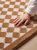 A child's hand touches the Little Forest Animals Silk Rug — The Diamond, highlighting its soft, raised texture and subtle diamond harlequin design in luxurious brown and beige tones.