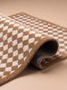 The Little Forest Animals Silk Rug — The Diamond is a beige and white checkered hand-tufted rug with a luxuriously soft texture, shown partially rolled to reveal its stylish patterned front and a dark, textured non-slip backing against a neutral background—ideal for bringing contemporary comfort to any modern child’s room.