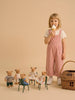 A young girl in pink overalls eats an ice cream cone, standing next to a rattan basket gift set. In front of her are five Little Forest Animals — The Thompson Family figurines, some sitting on small chairs, arranged as if at a tea party.