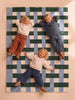 Three young children smile and lie on their backs, arms behind their heads, dressed in casual, comfortable earthy-toned clothing, on The Weave’s Little Forest Animals Silk Rug.