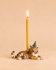 A lit yellow candle is held by the Tiger Cake Topper—a charming, hand-painted ceramic tiger figurine wearing a small blue party hat—set against a plain beige background, making it an adorable birthday decoration.