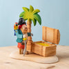 The Bumbu Handmade Wooden Treasure Hunt Set includes a pirate with a parrot, a palm tree, and an open treasure chest filled with gold on a light wooden base—ideal for eco-friendly and imaginative play.