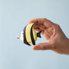 A hand holds a small, yellow, black, and white striped fish from the Bumbu Handmade Wooden Tropical Fish Set against a plain light blue background.