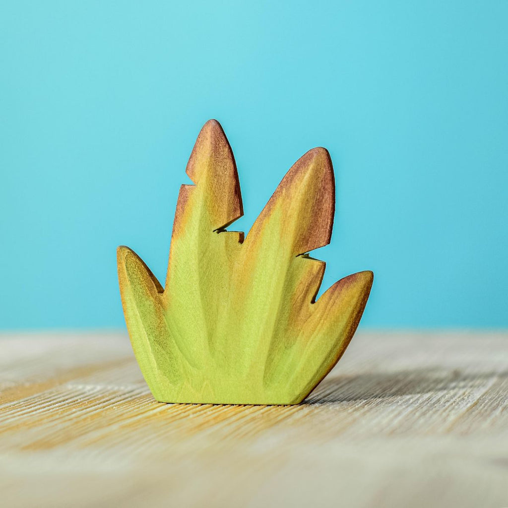 A wooden puzzle piece shaped like a Wooden Banana Bush in gradient colors from green to dark brown, made from lime wood and standing upright on a light wood surface against a soft blue background.