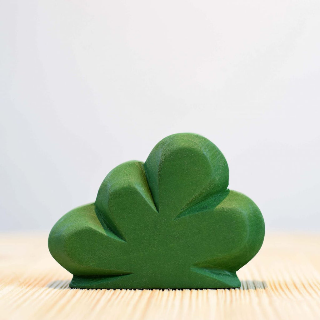 A green shamrock-shaped Wooden Large Green Bush sits on a wooden surface against a pale background, symbolizing Irish culture and good luck.