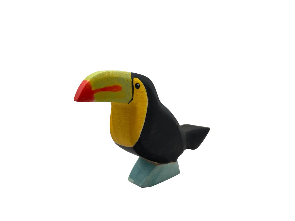 A high-quality Handmade Holzwald Toucan Bird sculpture with a bright yellow head, red beak, and black body, perched on a small blue base, isolated on a white background.