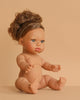The Minikane Baby Doll (13") - Melissa, an anatomically correct doll with curly brown hair, sits upright on a beige surface and background. Beautifully crafted and made in Spain. Clothing sold separately.
