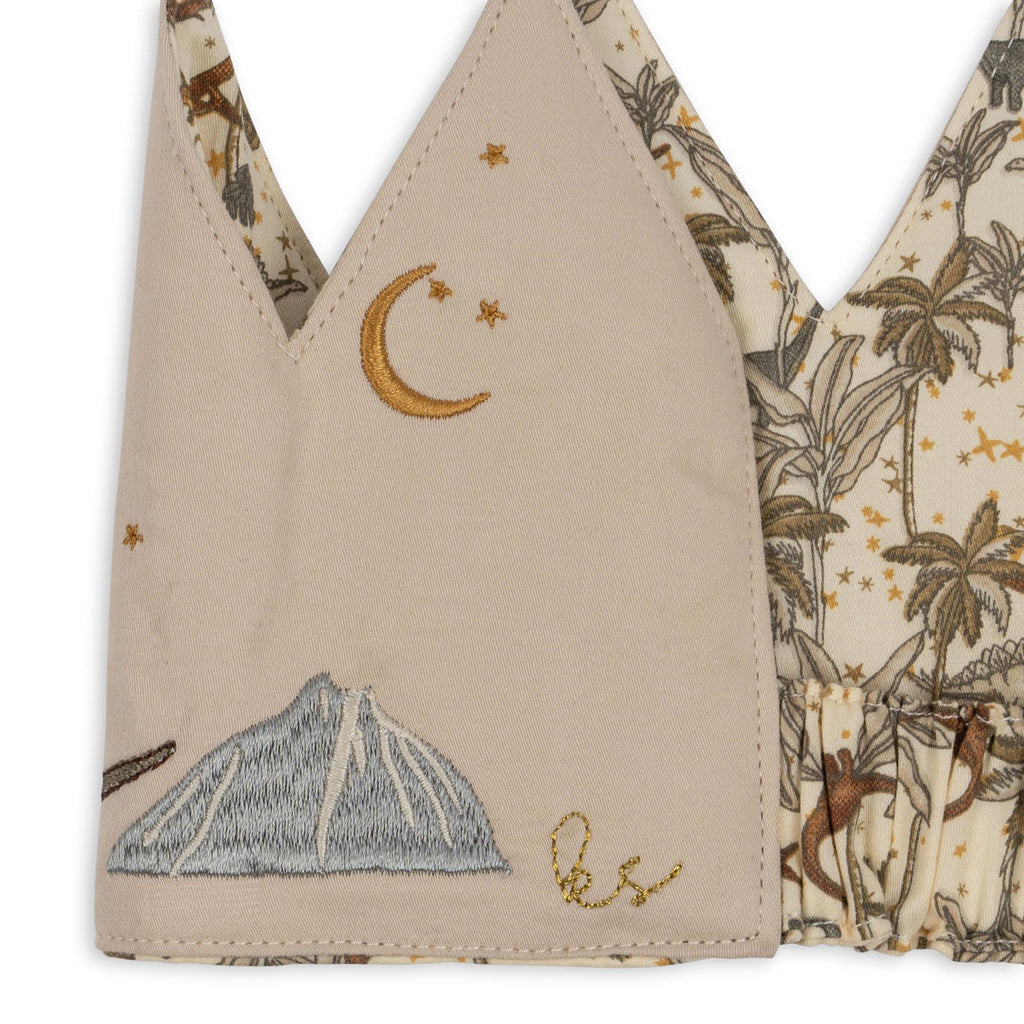 The Konges Sloejd Birthday Crown - Dino is a beige cotton crown with a tropical print background featuring monkeys, palm trees, and gold stars, plus embroidered crescent moon, blue mountain, yellow "LS" initials, and stars.