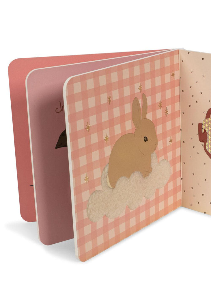 The Konges Sloejd Touch and Feel Book - Unicorn is open, revealing a page with a unicorn illustration on a soft cloud set against a pink checkered background dotted with small golden stars.