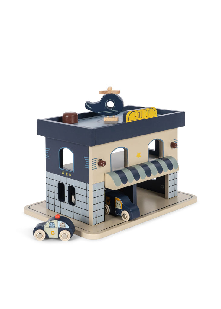 The Konges Sloejd Wooden Police Station, crafted from FSC-certified wood, features a blue and beige station with a police sign, an attached garage, two police cars, and a rooftop helipad for toy helicopters.