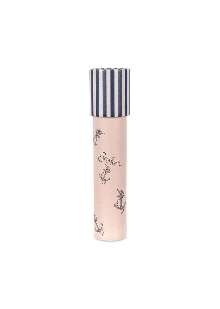 The Konges Sloejd Kaleidoscope - Rock My Boat is a pink cylinder featuring navy blue anchors, seahorses, and “Sailor.” Its navy and white striped top contains colorful pearls that shimmer as you turn the kaleidoscope.