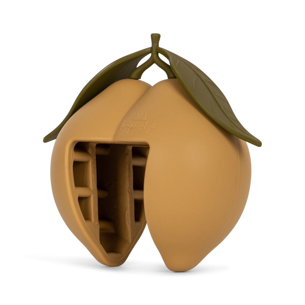 A CE-tested, lemon-shaped silicone door stopper by Konges Sloejd, light yellow with two green leaves on top, features a large cutout section revealing internal compartments.