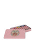 The Konges Sloejd Beeswax Crayons - Cherry Bow come in a pink tin box decorated with cherries and flowers, containing pastel non-toxic crayons neatly arranged inside. The lid is partially open and placed next to the box.