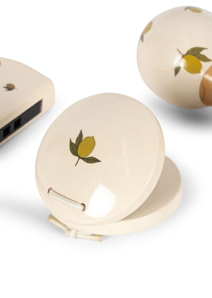 The Konges Sloejd Petit Music Set - Glossy Lemon features cream-colored circular castanets adorned with yellow lemons and green leaves, shown here on a white background.