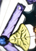 A close-up of the Konges Sloejd Kaleidoscope - Like Cats and Dogs reveals vibrant stained glass-style pieces—including a purple rectangle with a hole, a yellow-green leaf shape, and a teal fragment—all illuminated from behind to showcase their intricate textures and dazzling colors in a mesmerizing kaleidoscopic display.
