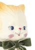 Close-up of the Konges Sloejd Money Bank - Kitty: a vintage-style ceramic cat figurine, handpainted with blue eyes, pink cheeks, a small smile, and a green velvet bow around its neck against a white background. This charming piece also serves as an adorable kitty money bank.