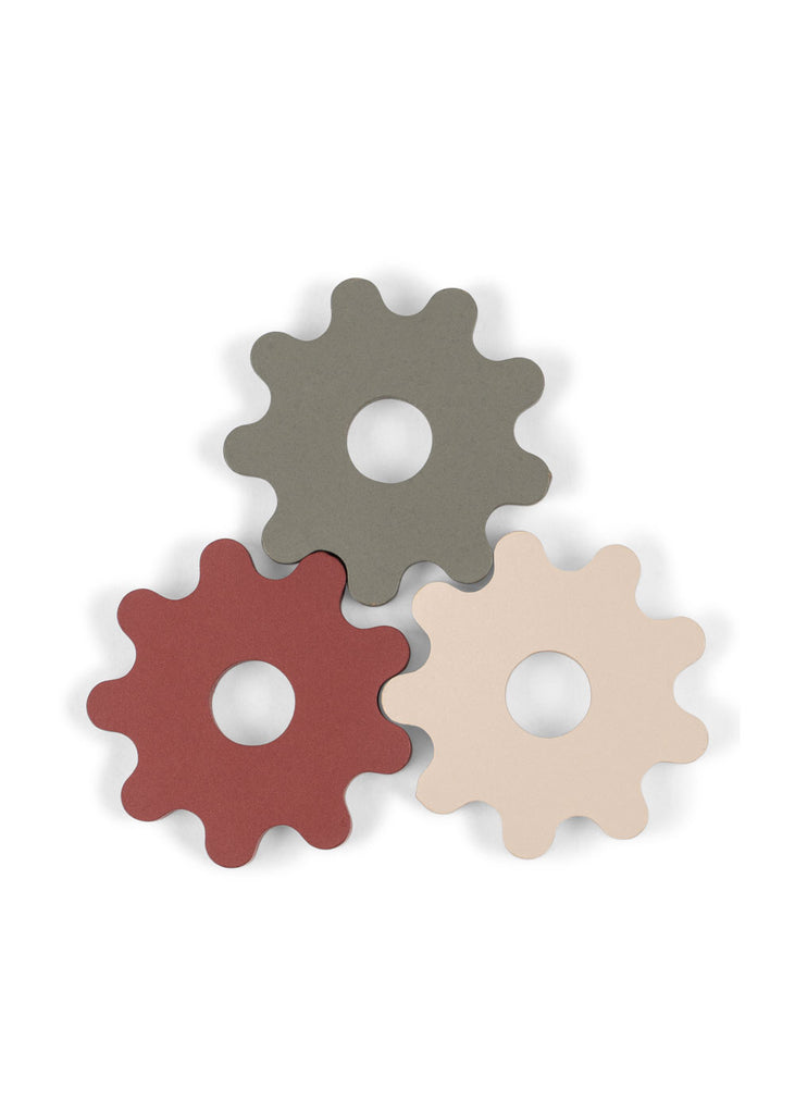 Three gear-shaped objects in gray, red, and beige overlap on a white background. Each has a circular hole in the center and rounded edges, resembling playful gears or toy parts—perfect components for the Konges Sloejd Tool Bench to inspire creative play with wooden toys.