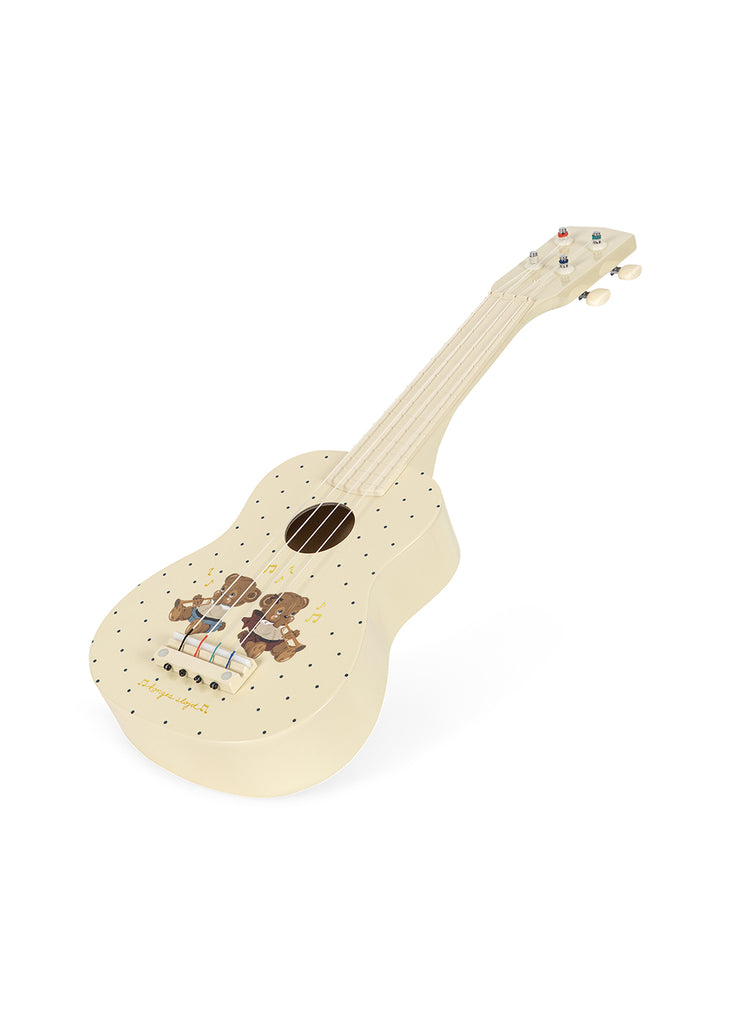 A small cream-colored Konges Sloejd Wooden Ukulele - Teddy Bear, adorned with whimsical teddy bear illustrations and scattered black dots, is photographed on a white background. This charming kids’ musical instrument is thoughtfully crafted to inspire young musicians.