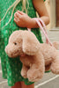 A child in a green dress stands on a stone path outdoors, holding the Konges Sloejd Puppy Bag by its pink strap.