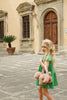 A young girl in a green dress with braided hair walks outside a historic building, holding a Konges Sloejd Puppy Bag.