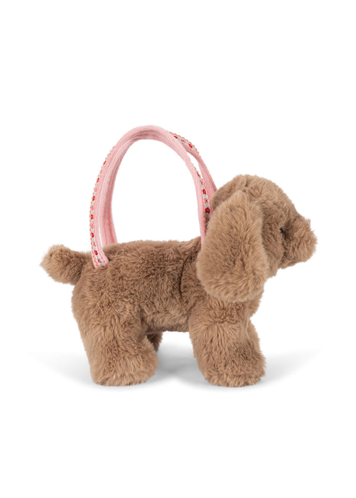 The Konges Sloejd Puppy Bag is a plush brown dog toy with floppy ears, standing on all fours and featuring a pink handle for use as an adorable kids handbag or playful puppy bag.
