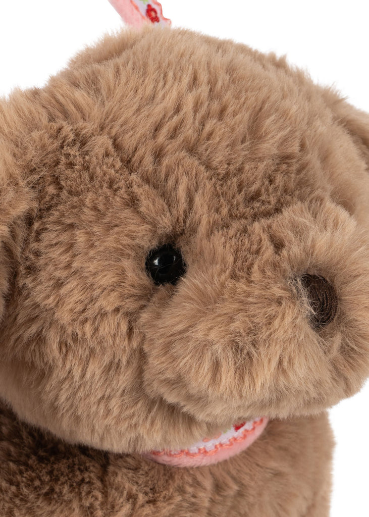 Close-up of the Konges Sloejd Puppy Bag shows its fluffy brown face, black plastic eyes, stitched brown nose, and soft fur. A pink and white ribbon completes this adorable kids handbag.