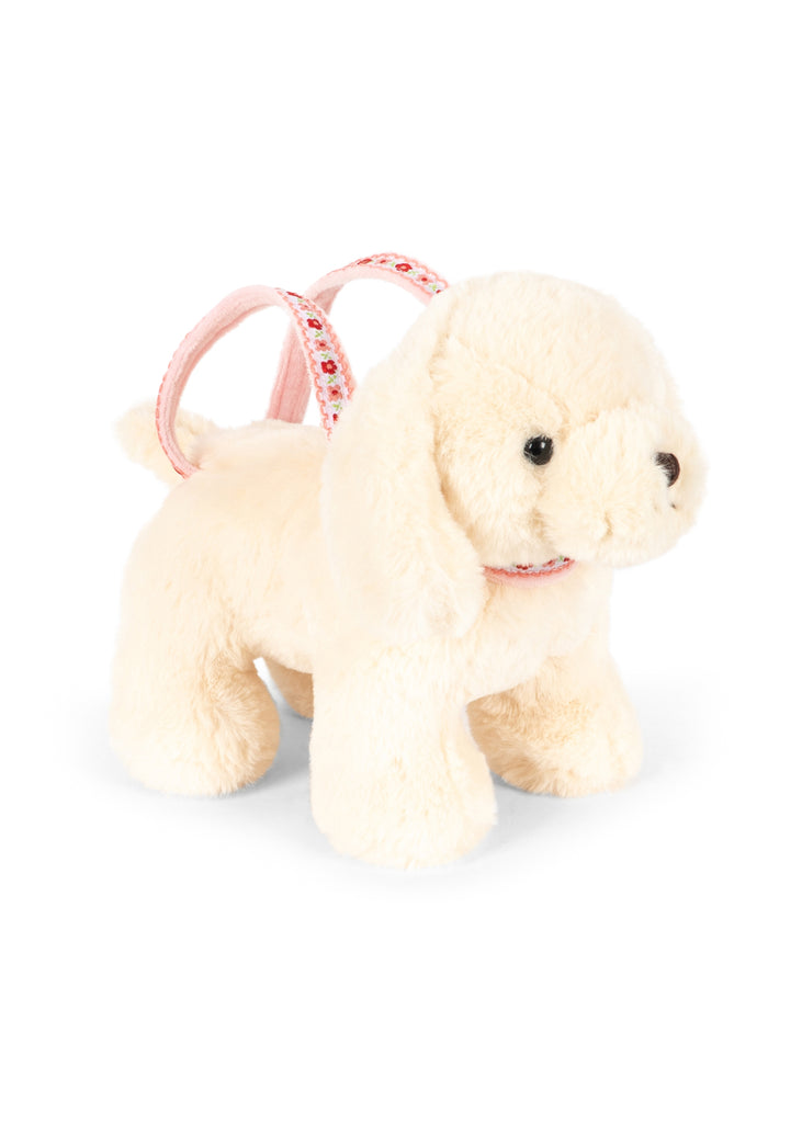 The Konges Sloejd Puppy Bag - Off White is a plush cream toy dog with black eyes and nose, featuring a pink floral harness, perfect as a cute bag for kids.