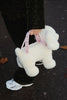 A child in dark clothes and white sneakers holds the Konges Sloejd Puppy Bag - Off White, standing on a leaf-strewn paved surface.