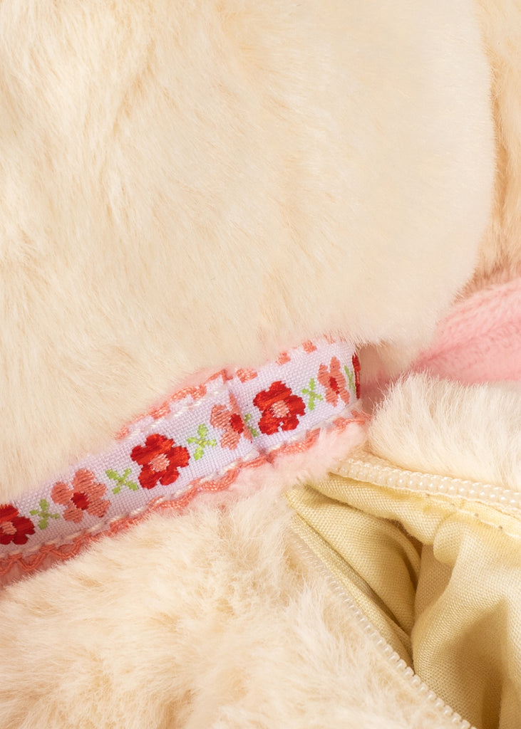 Close-up of the Konges Sloejd Puppy Bag - Off White’s cream fur with a white ribbon adorned with red flowers and green leaves, plus glimpses of light pink fabric and a cream zipper.
