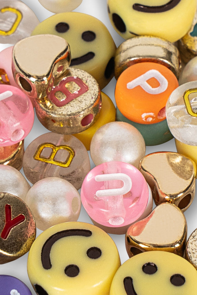 A close-up of the Konges Sloejd ABC Jewelry Set showcases smiley beads, gold accents, and letter pearls in pink, white, yellow, and orange—perfect for jewellery making.