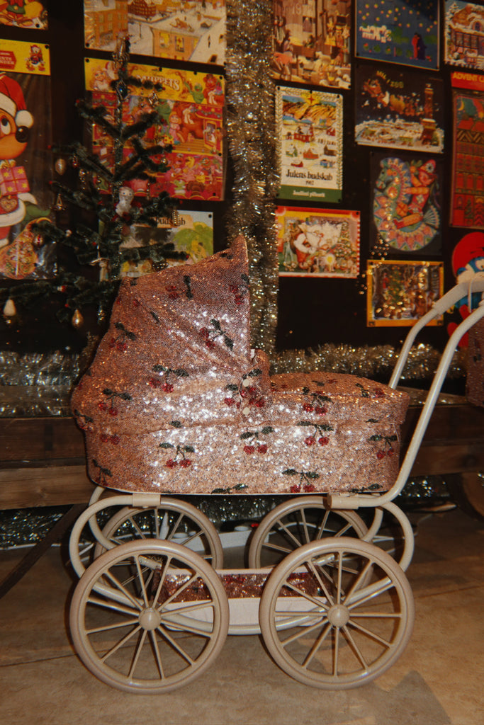 Konges Sloejd Mini Doll Pram - Sparkly Cherry Sequin featuring a vintage-style design with a sequined cherry pattern, set on a white frame with four wheels.