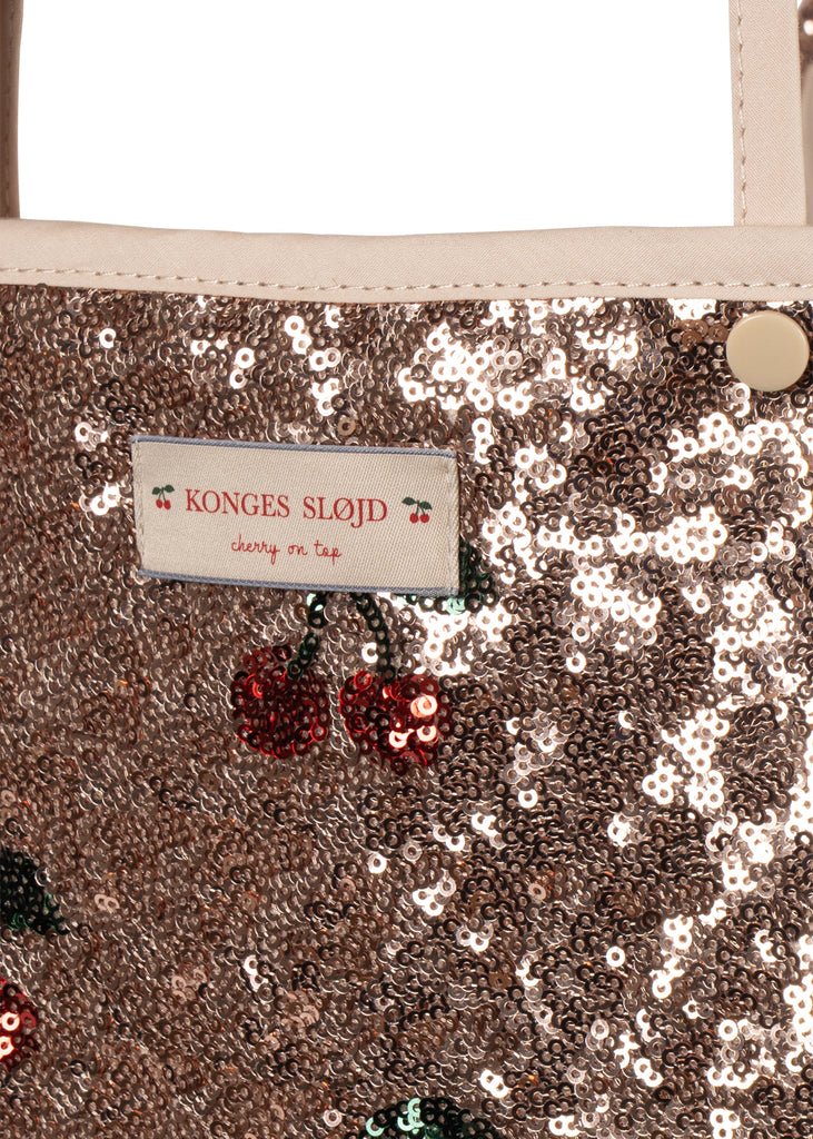 Rose gold sequined fabric featuring cherry-shaped sequins and a “Konges Sløjd cherry on top” label, shown here on a Konges Sloejd Mini Doll Pram - Sparkly Cherry Sequin.