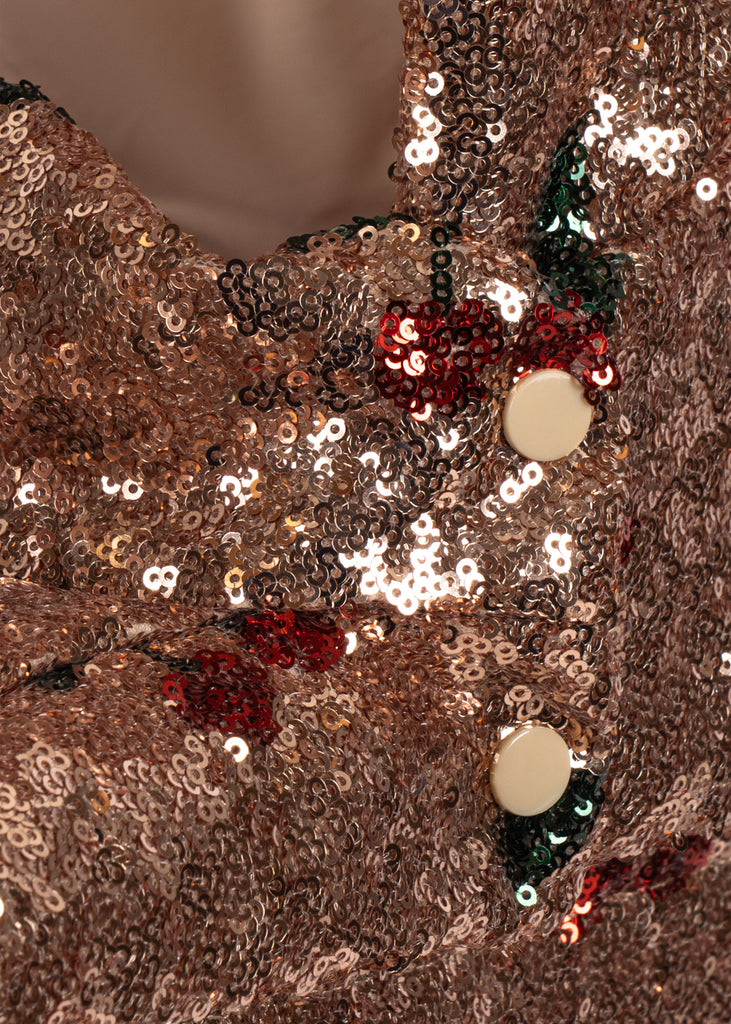 Close-up of fabric from a Konges Sloejd Mini Doll Pram - Sparkly Cherry Sequin, covered in gold sequins with red cherry patterns and two round cream-colored buttons.