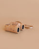 The Konges Sloejd Explorer Binoculars - Cherry, featuring adjustable focus and a matching strap, are displayed on a plain beige surface adorned with small colorful dots.