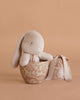 A Maileg Easter Egg with Bunny is displayed in a decorative beige bowl with floral patterns, beside a matching round gift box tied with a beige ribbon, all set against a beige background.