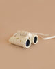 The Konges Sloejd Explorer Binoculars - Lemon, featuring a white lightweight design with a neck strap and lemon pattern, rest on a plain light beige surface against a soft, matching beige background.