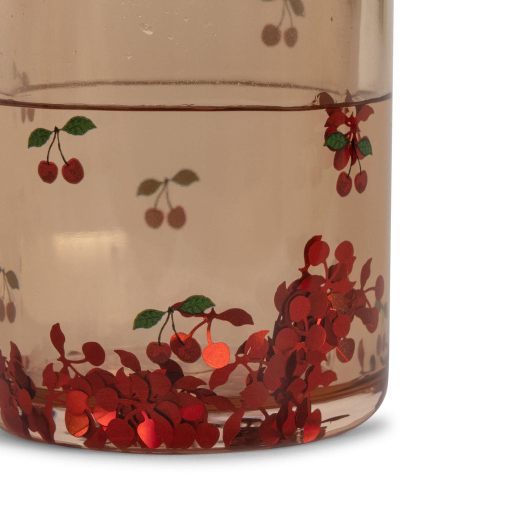 Close-up of Konges Sloejd Glitter Cups - Cherry (2 Pack): transparent glass cups with red cherry and green leaf illustrations. Playful cherry clusters at the bottom make them perfect for fun kids’ drinkware or lively dinnerware collections.