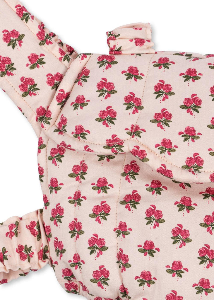 A close-up of the Konges Sloejd Doll Carrier - Rosie Rose, a quilted cotton bag with pink floral patterns on a cream background, featuring a flap and ruched straps—a charming toy accessory for any little one.