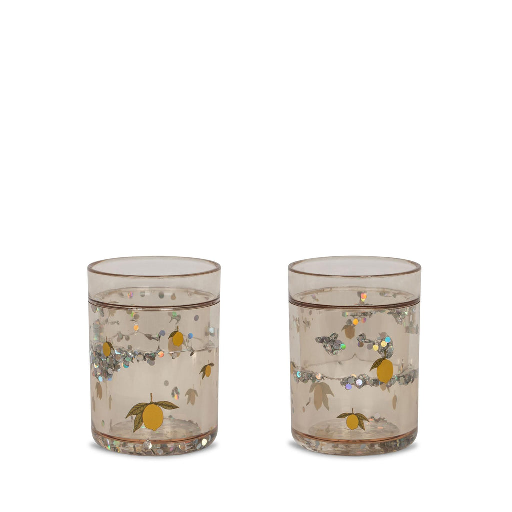 The Konges Sloejd Glitter Cups - Lemon (2 Pack) feature a subtle brown tint, yellow lemons, green leaves, and glittery dots—fun, stylish drinkware that brightens any table and is perfect for kids.