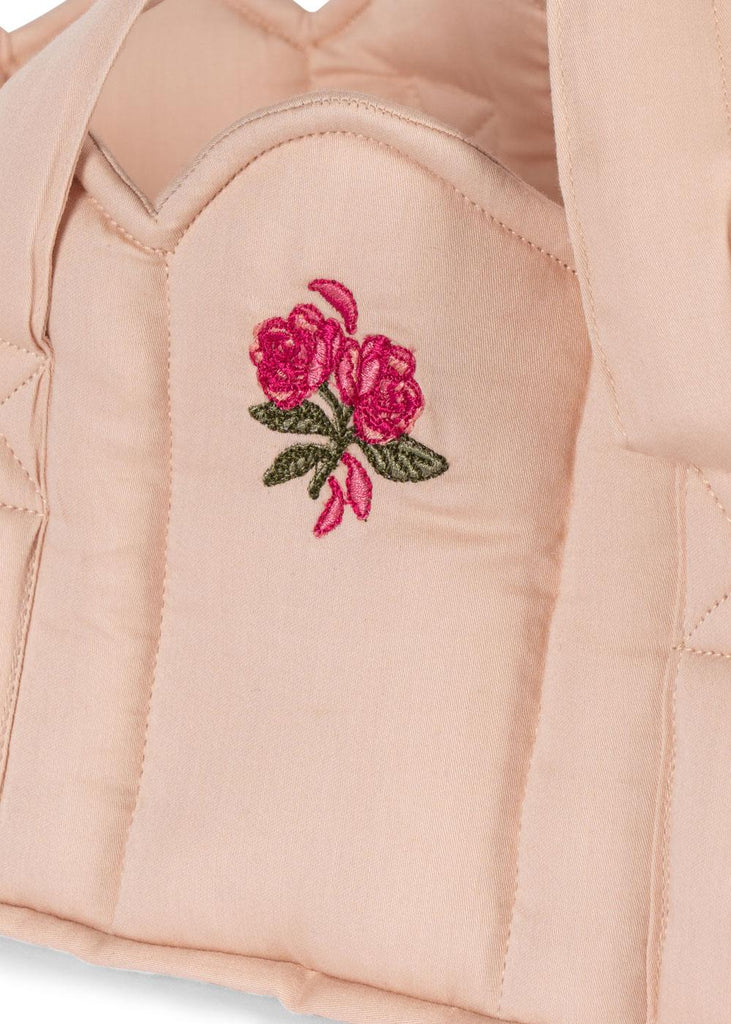 A close-up of the Konges Sloejd Doll Lift in Cameo Rose, showcasing its light pink quilted cotton fabric with an embroidered motif of two pink roses and green leaves at the center.