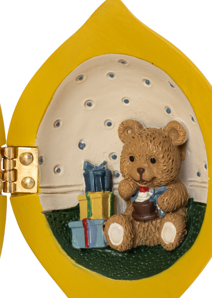 A Konges Sloejd Mini Surprise House - Lemon shaped hinged ornament opening to reveal a miniature world with a teddy bear holding a cupcake next to two wrapped gifts.