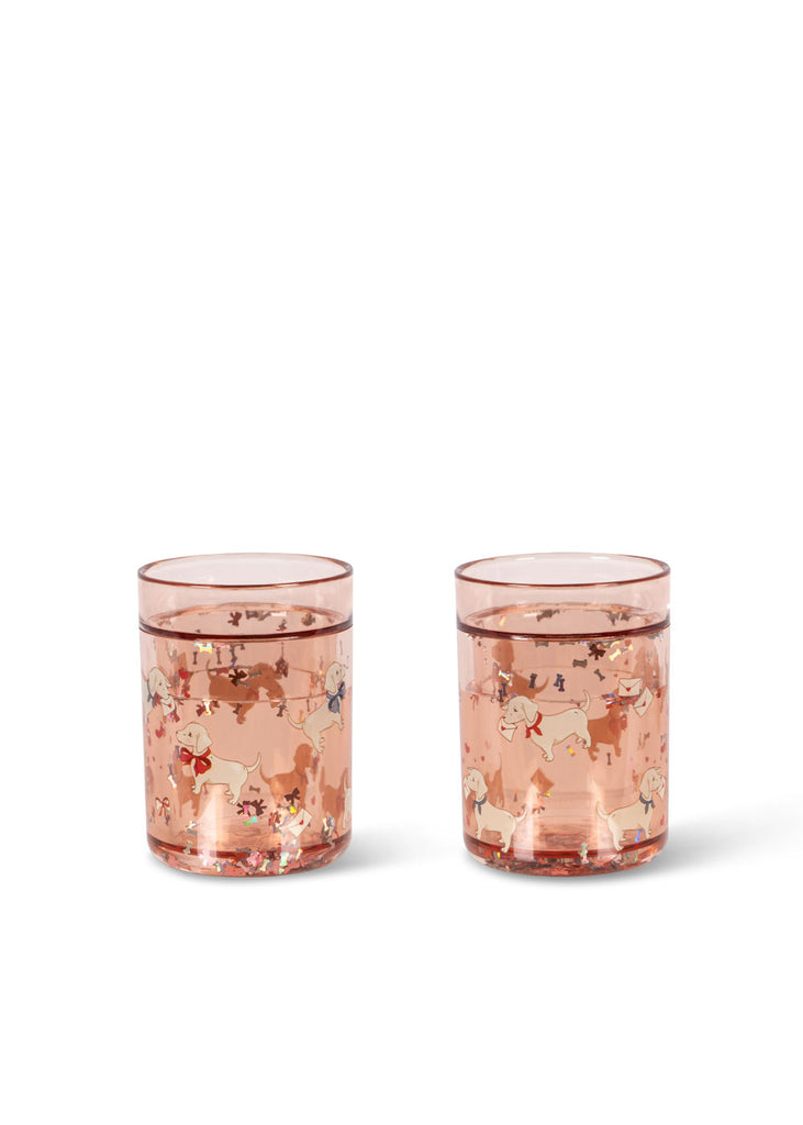 A Konges Sloejd Glitter Cup - Woof Letter Rose, a pink cup with playful dog illustrations and small stars, is photographed on a white background.
