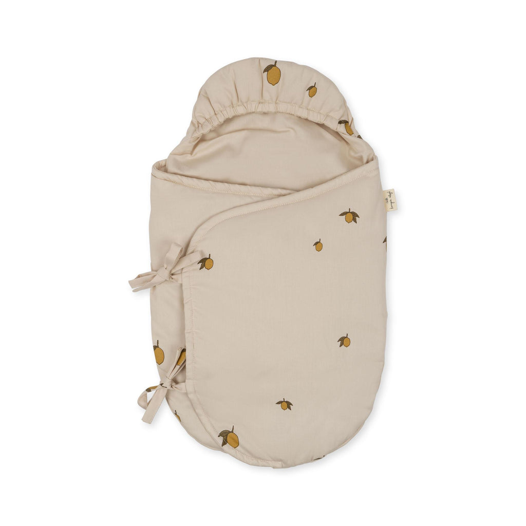 The Konges Sloejd Doll Sleeping Bag - Lemon is a beige swaddle with a hood, made from organic cotton and decorated with a small lemon print. It features two side ties to secure the wrap.