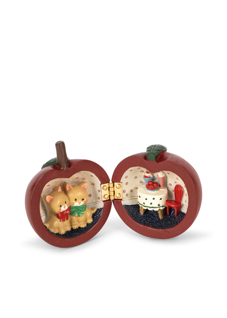 The Konges Sloejd Mini Surprise House - Cherry is an apple-shaped trinket box that opens to reveal a miniature world, with two kittens in one half and a tiny table and chair in the other.