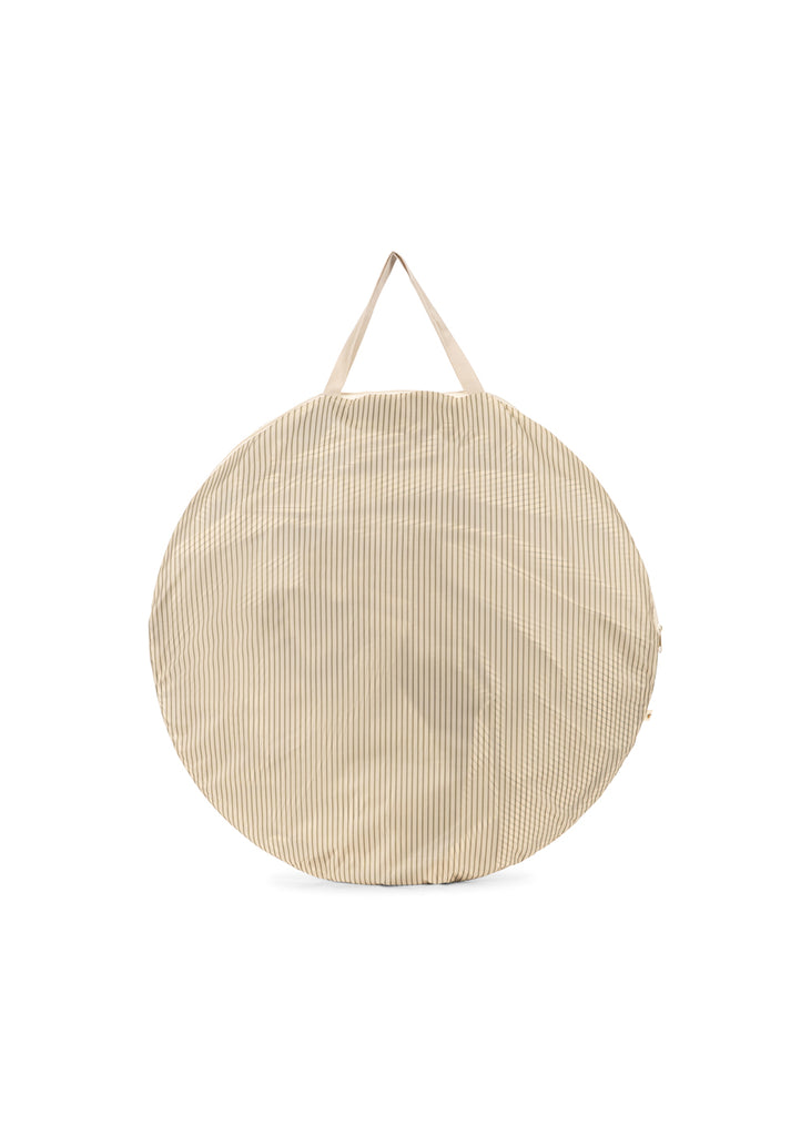 The Konges Sloejd Pop-Up Beach Tent UPF 50+ comes in a large, round bag with thin beige and white vertical stripes, two short beige handles, and a soft, slightly textured surface for easy portability.