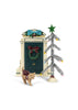 A Konges Sloejd Christmas Door miniature decorated with a wreath and a blue bow, standing next to a small silver tinsel Christmas tree and a toy cat wearing a maroon bow.