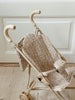 The Konges Sloejd Doll Stroller - Milk Tank, featuring soft handles and a floral-patterned fabric seat in beige, is positioned on a light wooden floor in front of a white paneled door. Its double wheels offer enhanced stability, making it ideal for playtime adventures.